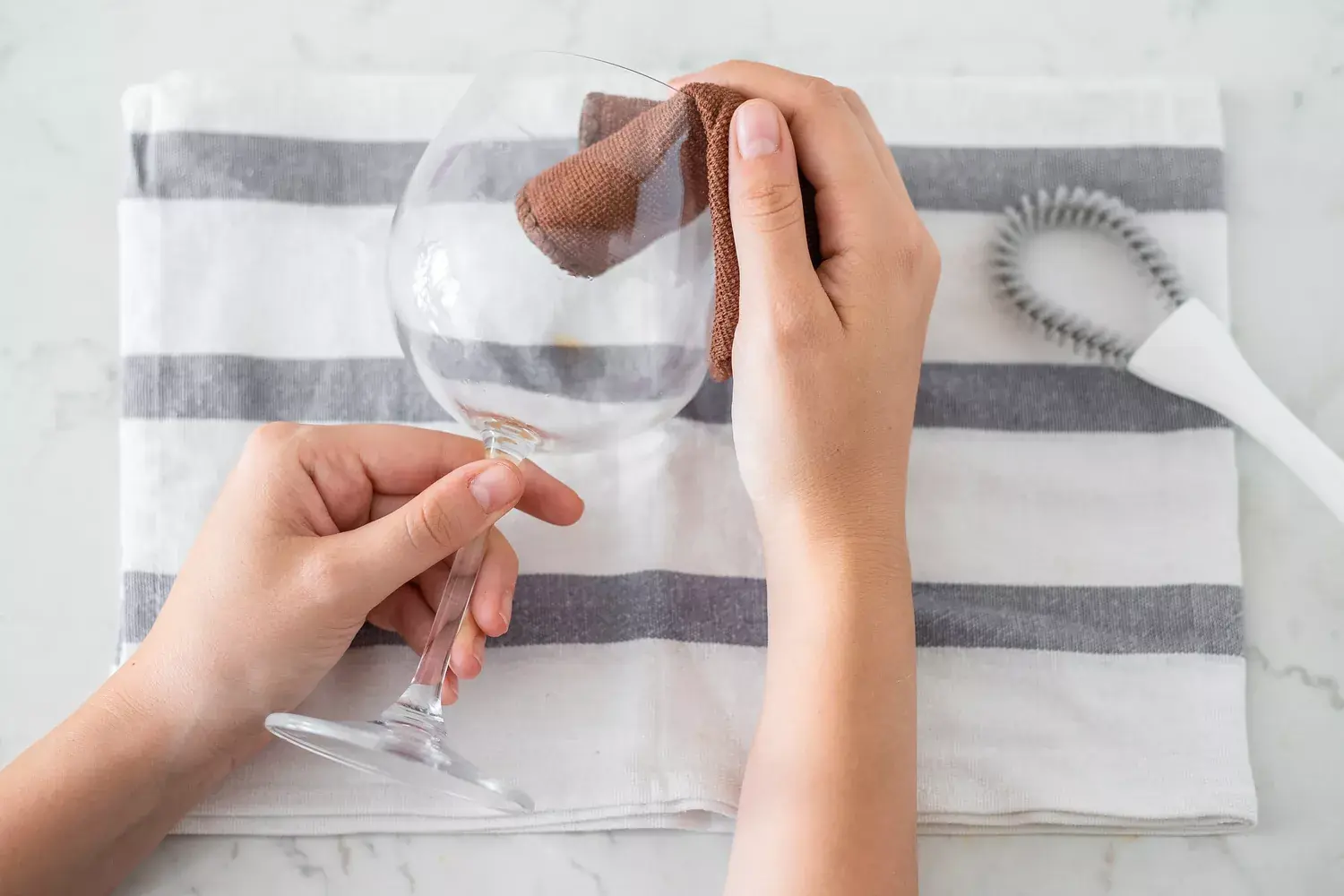 Wine glass being wiped with brown cloth over striped napkin